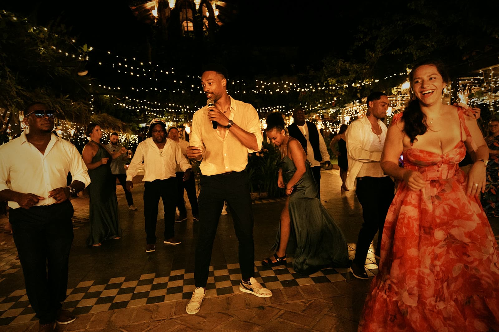 DJ Keybo leading the dance floor with a mic under string lights